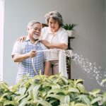 Elderly Couple Watering A Flower In Home Garden