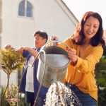 Mature Asian Couple At Work Watering And Pruning Plants In Garden At Home