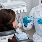 Cropped View Of Dentist In Latex Gloves Holding Toothbrush Near Teeth Model And Girl
